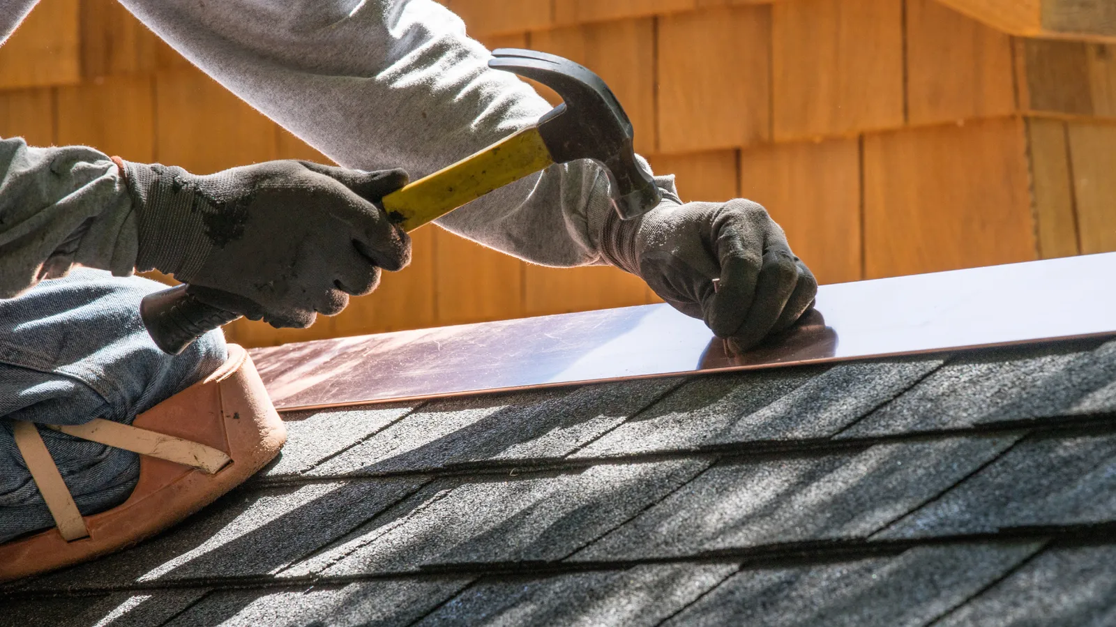 A roofer hammering metal flashing along a shingle roof edge