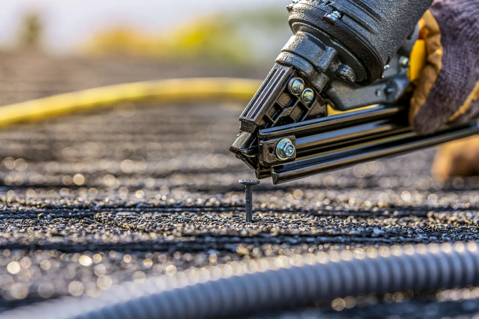 A roofer using a pneumatic nail gun to nail down asphalt shingles