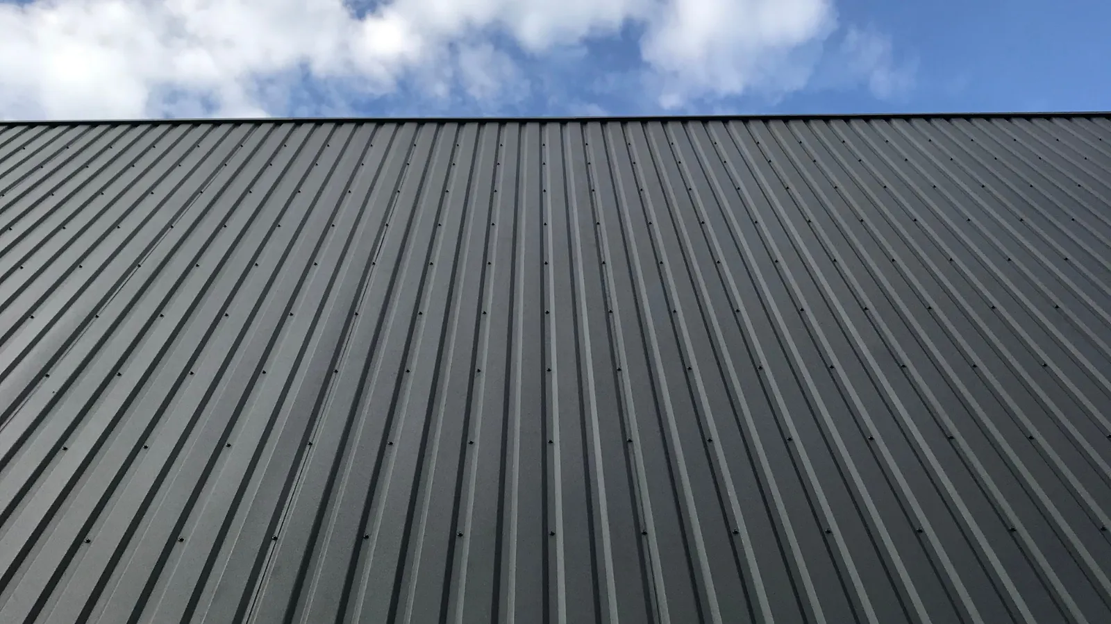Dark ribbed metal panels rising toward a partly cloudy sky