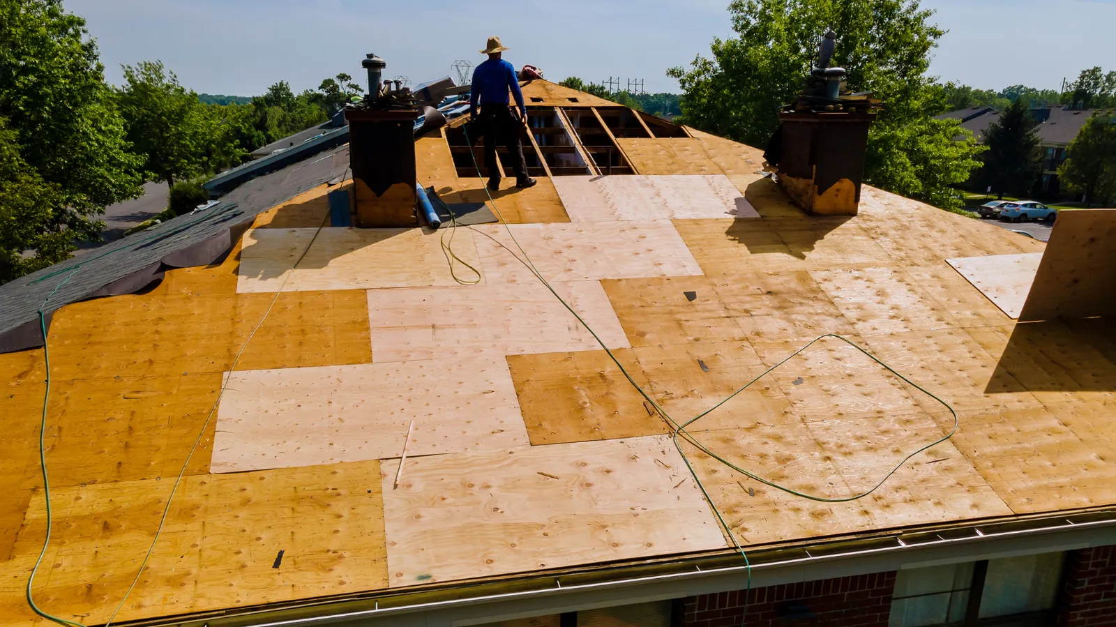 Large roof covered in new plywood decking where a roofer stands